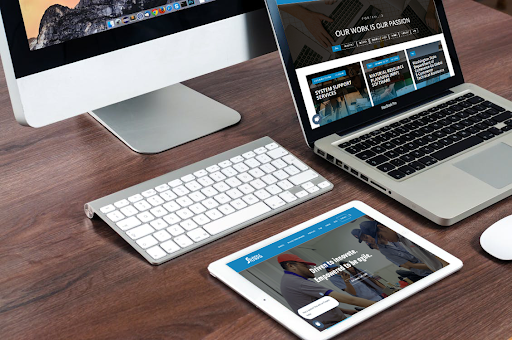 A responsive website displayed on an iMac, MacBook, and iPad, demonstrating accessible web design across multiple devices on a wooden desk.